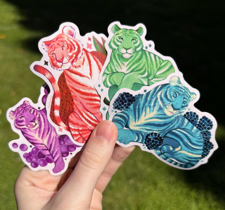 Fruit Tigers Image of a hand holding 4 vinyl stickers, each featuring a different tiger inspired by fruit. From left to right there is a purple grape tiger, pink strawberry tiger, green apple tiger, and a blue raspberry tiger.