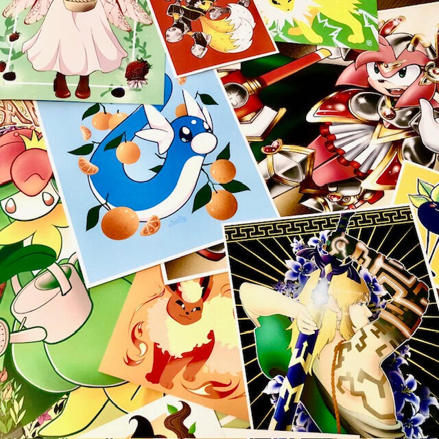 Assorted Art Prints Image of various art prints from lots of fandoms, shows and games all piled together on a table.