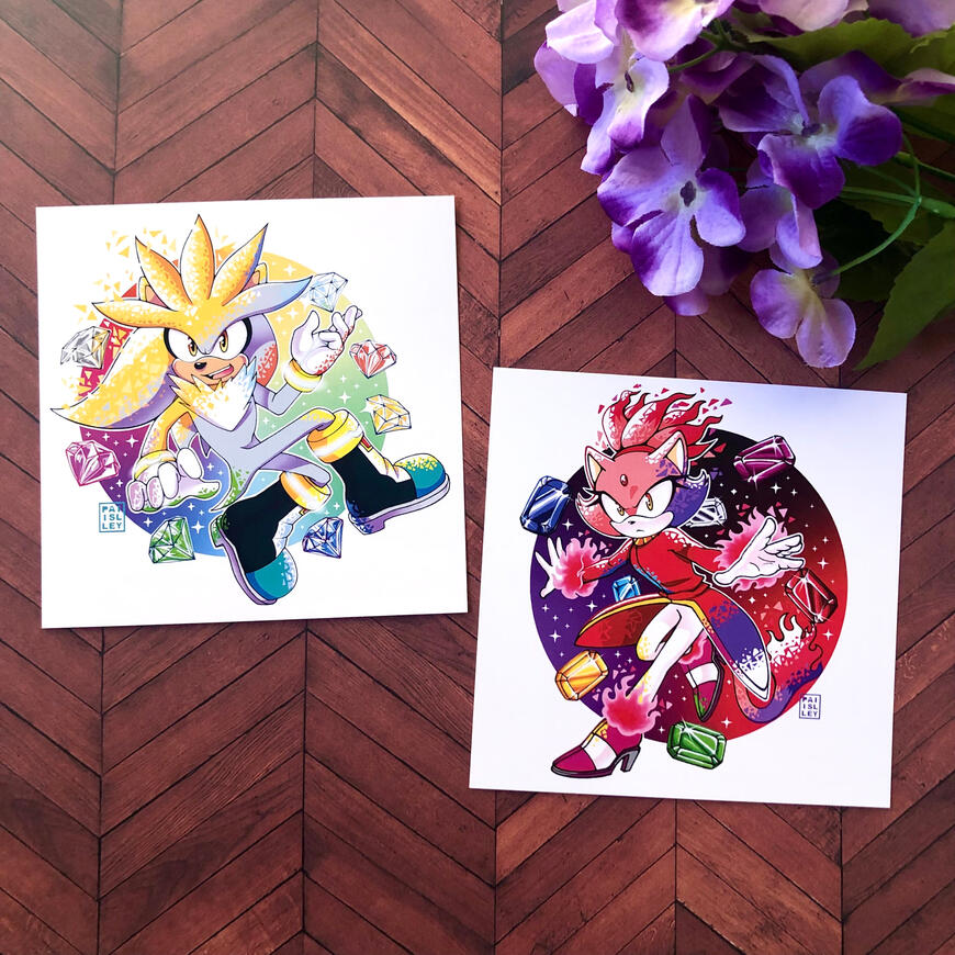 Sonic Prints 2 Image of 2 art prints, left featuring Silver floating surrounded by the 7 chaos emeralds, right features Blaze the Cat, her arms outstretched surrounded by the Sol Emeralds. Both are turning into their super forms.