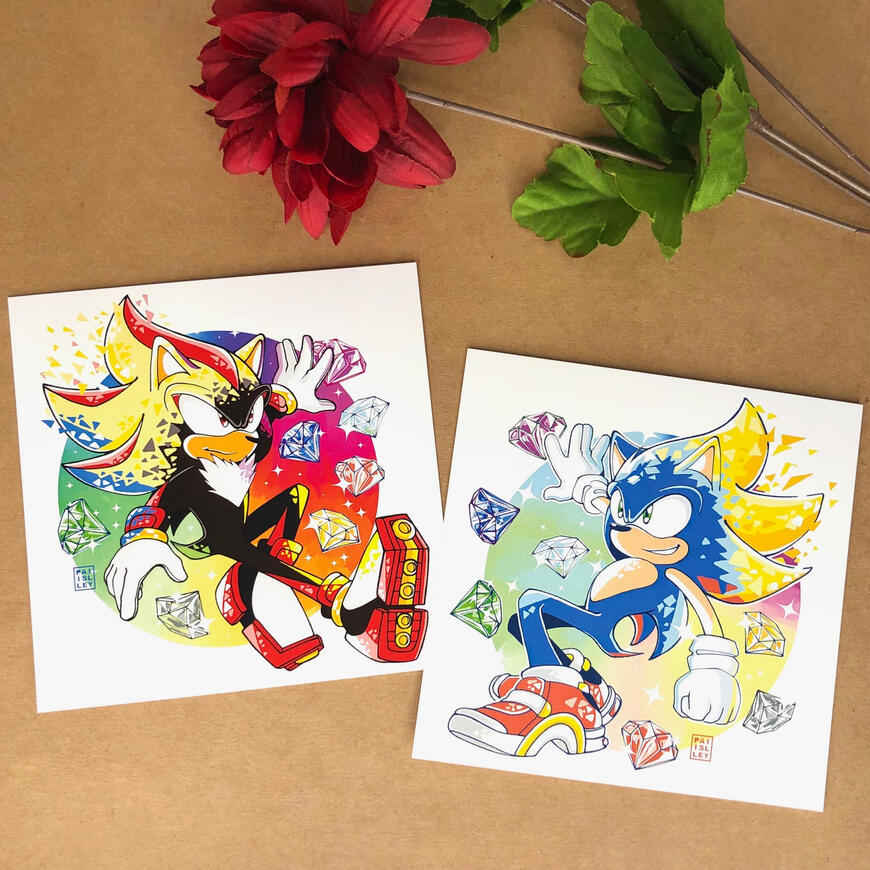 Sonic Prints Image of 2 prints, left featuring Shadow the Hedgehog with all 7 chaos emeralds floating around him going super, and the right features Sonic the Hedgehog with all 7 chaos emeralds going super. Both quills are turning gold